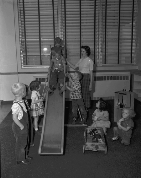 A woman looking after children as they go down an indoor slide.