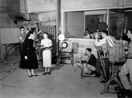 Students operating broadcasting equipment and reading scripts for television broadcasting class.