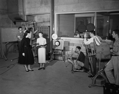 Students operating broadcasting equipment and reading scripts for television broadcasting class.