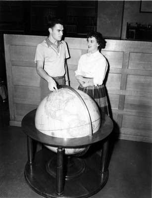 Two students looking at a large globe and pointing to an area in Canada.
