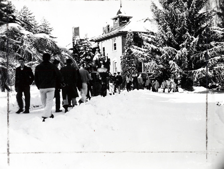 A large number of students walking along a snowy path between buildings.