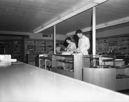 Two employees are behind the counter in the University of Idaho bookstore, a student can be seen in the background.