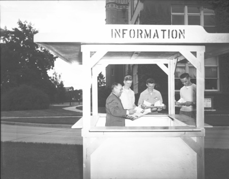 A photograph of new students standing at an information kiosk outside.