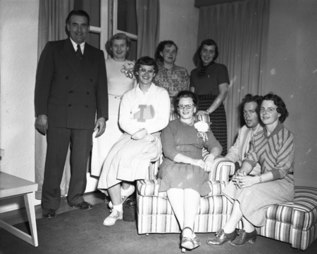 A group of women and men pose for a photograph. A cheerleader wearing her cheerleading outfit sits in the middle.