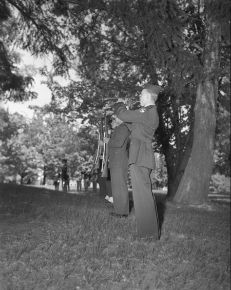 ROTC members in line and holding their rifles. The member closest to the camera plays a brass instrument.