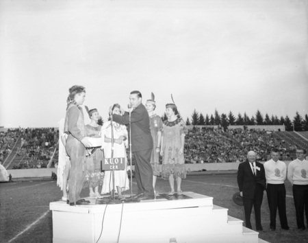 Governor Smylie at the Homecoming game, speaking surrounded costumed students in the football stadium.