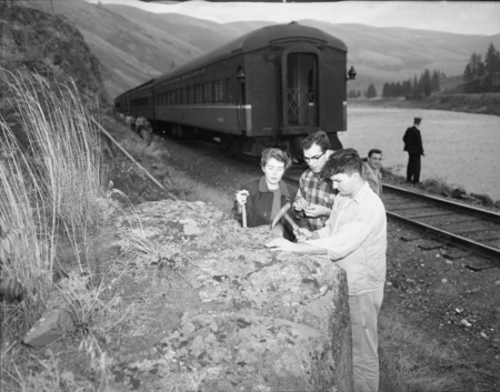 Students use their rock hammers to get a sample from a boulder.