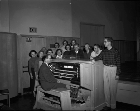 Choir practice being led by Music Department faculty Hall McInTyre Macklin at his three tier piano.