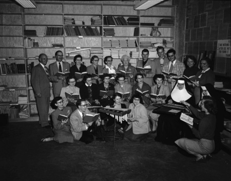 Choir students and faculty sing together from a song book.