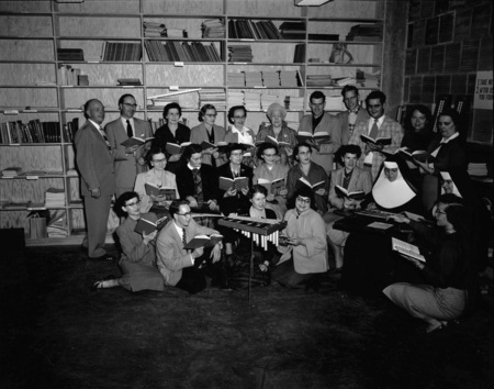 Choir students and faculty sing together from a song book.