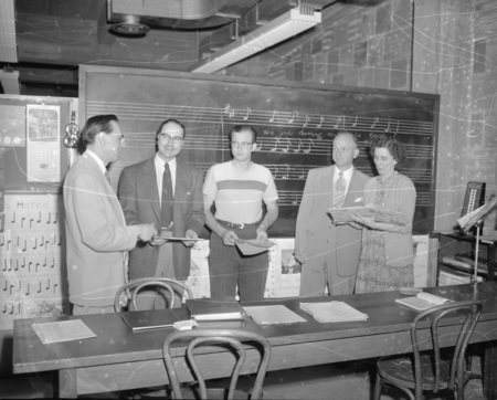 Music Department faculty member Hall McInTyre Macklin discussing a book of music with a group of people.
