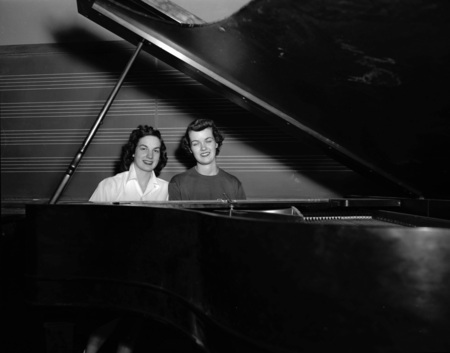 Music students Phyllis Grocke and Jane Bostic sitting at a piano in front of a blackboard, both former Miss Idaho.