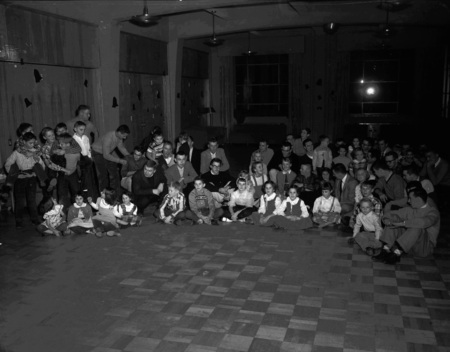University of Idaho's Interfraternity Council (IFC) Christmas party for Moscow children. Children are shown singing around a piano with the IFC members.