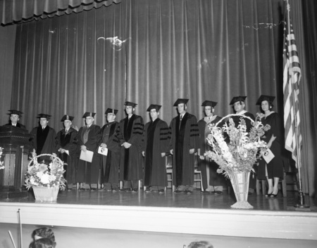 Students and faculty standing on a stage at the first commencement of the newly named Lewis-Clark State College.