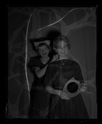 High school student holds her awards from a journalism conference while a women helps her with her necklace.