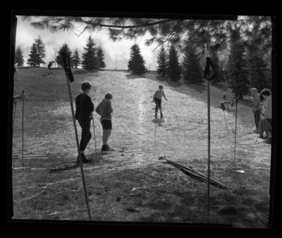Students in ski class practice going downhill on skis without snow in a grassy field.