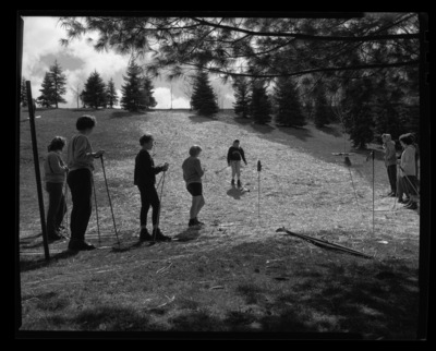 Students in ski class practice going downhill on skis without snow in a grassy field.
