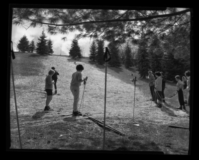 Students in ski class practice going downhill on skis without snow in a grassy field.