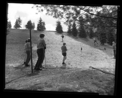 Students in ski class practice going downhill on skis without snow in a grassy field.