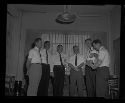 Six men stand together looking over a binder at the Idaho's Grocer's Conference at the University of Idaho.