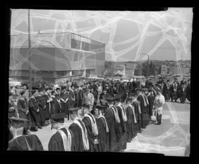 The Academic Parade walks up the stairs into Memorial Gym for Commencement. The Library building, greenhouses, and Ag Science building can be seen in the background.