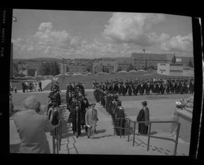 The Academic Parade ascends the steps of Memorial Gym for commencement. From left to right the Library, Ag Science, Gault Hall, Phinny and Brink Halls, the Small Animals Laboratory, and the Agronomy Building can bee seen in the background.
