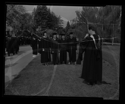 Graduates posing in cap and gown on the north lawn outside the Administration Building.