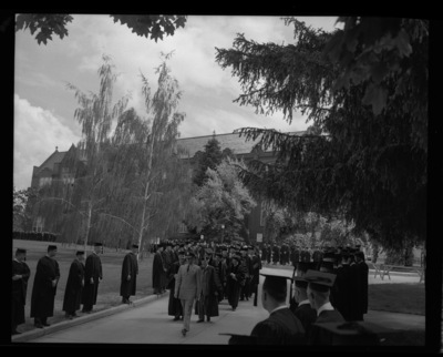 The Academic Parade leads the traditional commencement walk from the Administration Building to Memorial Gym. Behind the Military personnel is Governor Smylie (left) and President Theophilis (right).