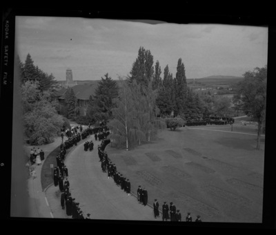 Students in cap and gown line Campus Drive outside of the Administration Building for the traditional walk from the Administration Buiding to Memorial Gym on commencement day.