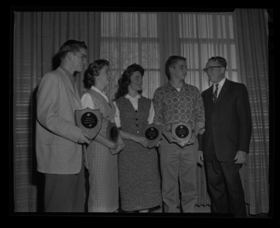 Four high school students hold the plaques their school paper was awarded for writing at the journalism conference by Dr. Granville Price, Chair of Journalism, at the University of Idaho. Left to right the Boise High Lights won the plaque for Service to School, The Moscow Wocsomanian won best feature stories, the Bonner's Ferry Badger won Best News Writing, and the Lewiston Bangal's Purr won for best sports section.