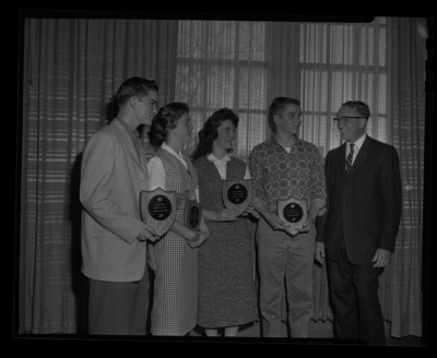 Four high school students hold the plaques their school paper was awarded for writing at the journalism conference by Dr. Granville Price, Chair of Journalism, at the University of Idaho. Left to right the Boise High Lights won the plaque for Service to School, The Moscow Wocsomanian won best feature stories, the Bonner's Ferry Badger won Best News Writing, and the Lewiston Bangal's Purr won for best sports section.