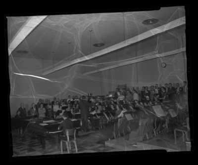 Choir being led by a director with piano player in the foreground.