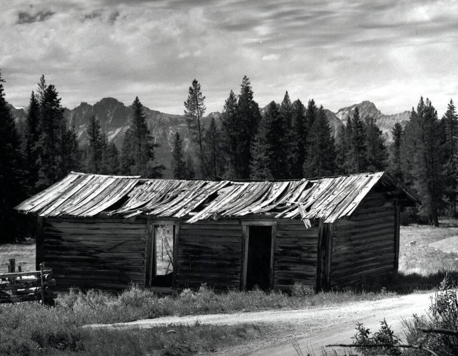 A dilapidated, abandoned cabin entered into the Boise Camera Club and received a score of 24 competition. It sits near a treeline with mountains in the background.