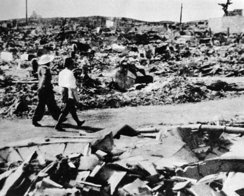 Photograph of two people walking along a path through the rubble left by the destruction of the atomic bomb.