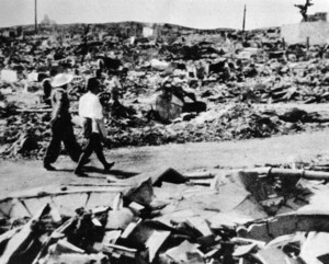 Photograph of two people walking along a path through the rubble left by the destruction of the atomic bomb.