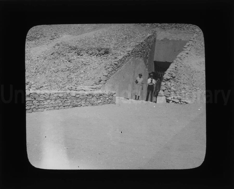 Two women and a man standing at the entrance of what appears to be a tomb in the style of the pyramids.
