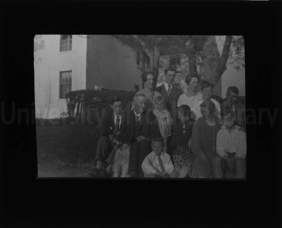 Group of men, women, children, and a dog posing outside a residential building. No individuals able to be identified.