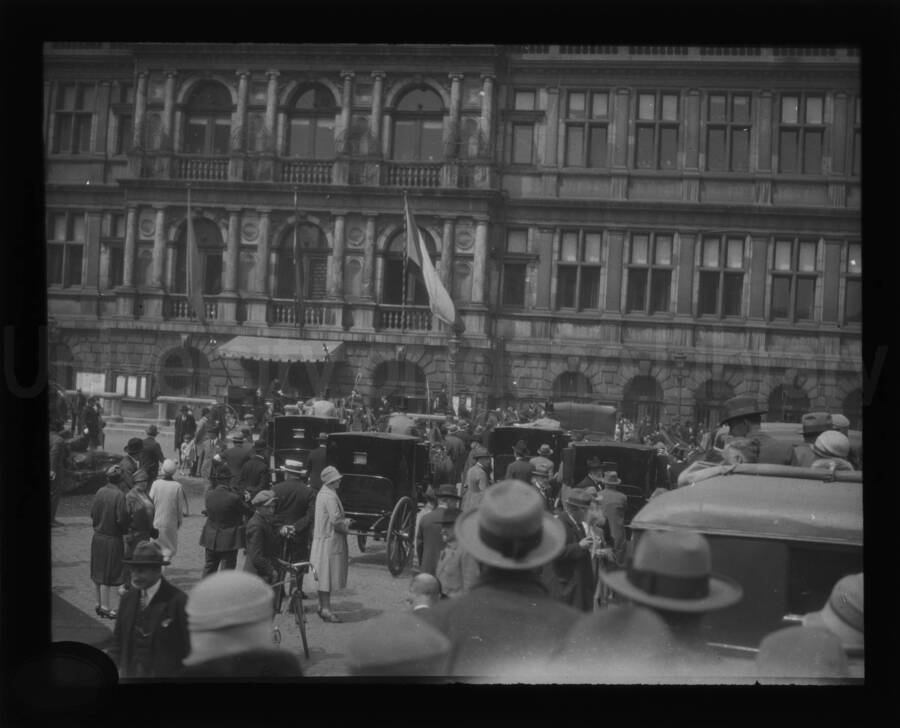 People and cars gathered in front of a building in an unknown location.