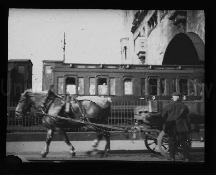 A train coming out of a tunnel with an open carriage pulled by horse in the foreground.