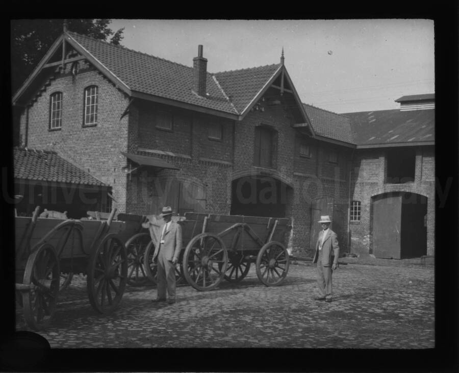 Four-wheeled carts and two men wait in front of a building.