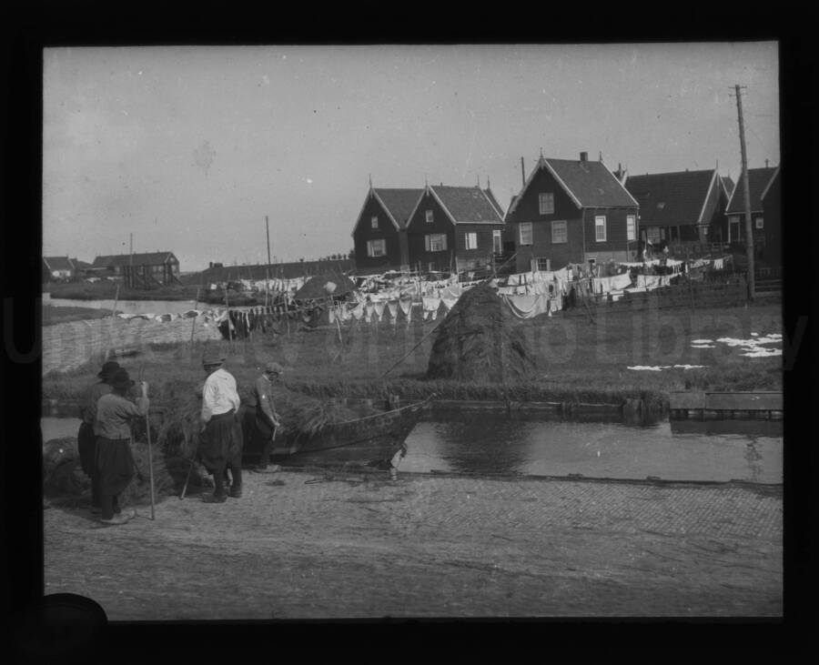 Men loading a boat in a canal with houses and clothing hanging on line drying.