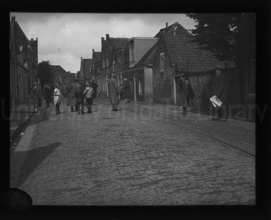 Street scene in an unknown location. rail tracks can be seen in the street with people walking away from the photographer.