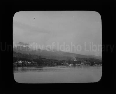 Mountains, boats, and buildings from an unknown location with a body of water in the foreground.