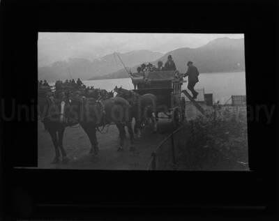 A man embarking in a four-wheeled carriage pulled by horses, followed by other similar carriages, near a shore.