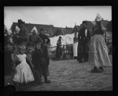 Maud Iddings poses with two children alongside several persons wearing traditional costume. (Netherlands?)