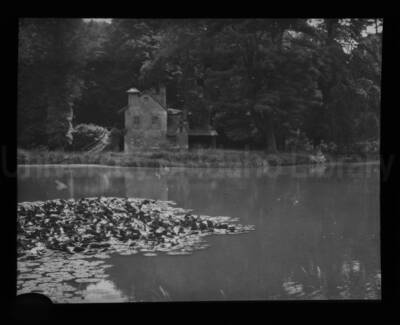The backside of a house in an unknown location with a body of water in the foreground of the photograph.