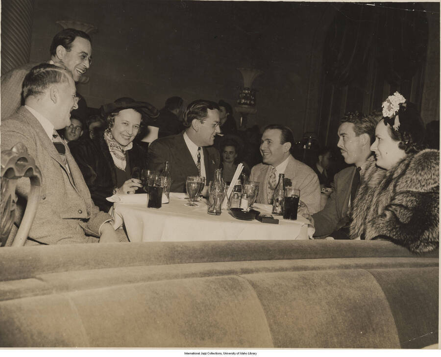 8 x 10 inch photograph; Glenn Miller, Charlie Spivak, and unidentified persons in a restaurant. Stamped on the back of the photograph: George B. Evans, NY