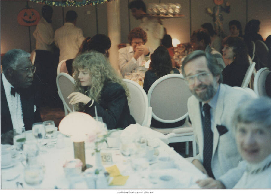 4 x 5 3/4 inch photograph; unidentified persons at a dinner table: [Scate Alsop?] and others; the man on the left with white hair and in the tuxedo is singer Joe Williams