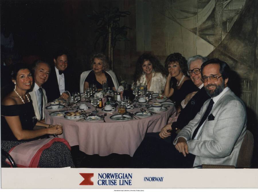 5 x 6 3/4 inch photograph; group of people at a dinner table. Handwritten on the back of the photograph: Diane and John McDevough?, Katie Pamell, Angela?, Mel P., Scate Alsop?, Jane and Leonard Feather. Inscription at the bottom of the photograph reads: Norwegian Cruise Line