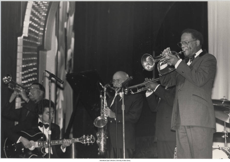 4 x 6 inch photograph; Adolphus "Doc" Cheatham on trumpet,  playing the flugelhorn, is Clark Terry and unidentified guitarist and saxophonist, performing